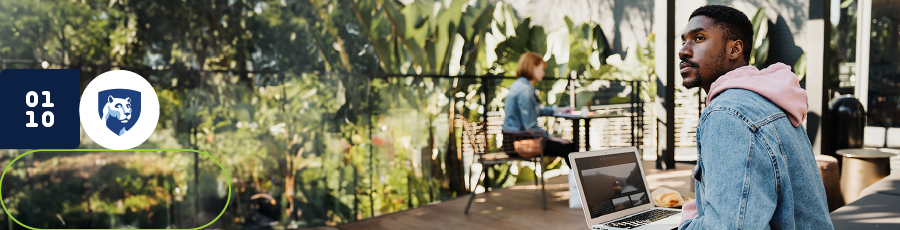 Individual sitting at a table with a laptop in an outdoor area with plants and glass panels