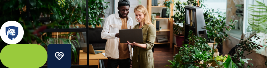 Two individuals in an indoor space with plants, one holding a laptop and gesturing towards it.

